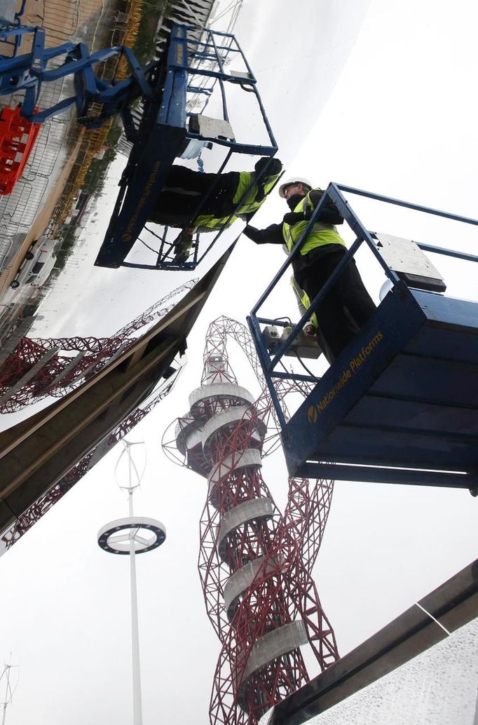 Workers install a large convex mirror which reflects the Olympic Stadium at a sponsor's stand in Stratford, east London, July 14, 2012. The London 2012 Games are due to open in less than two weeks. REUTERS/Andrew Winning (BRITAIN - Tags: SPORT OLYMPICS BUSINESS EMPLOYMENT) Published: Čec. 14, 2012, 1:52 odp.