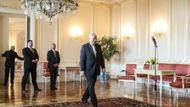 Z protějších dveří přichází prezident se svojí suitou.