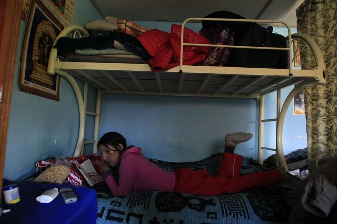 Marathon runner Gladys Tejeda, the first Peruvian athlete who qualified for the 2012 London Olympic Games, reads on her bead at her home in the Andean province of Junin May 14, 2012. A private company will take Gladys' mother Marcelina Pucuhuaranga, 69, to London as part of the "Thank you Mom" program. For Pucuhuaranga, who received her first passport, it will be the first time travelling out of Peru. The program will take about 120 mothers of different athletes around the world to attend the games. Tejeda, the youngest of nine children, returned to her hometown to visit her mother and to focus on training where she will run more than 20 km every day in the highlands (over 4,105 meters above sea level). Picture taken May 14, 2012. REUTERS/Pilar Olivares(PERU - Tags: SPORT ATHLETICS OLYMPICS) Published: Kvě. 17, 2012, 7:08 odp.