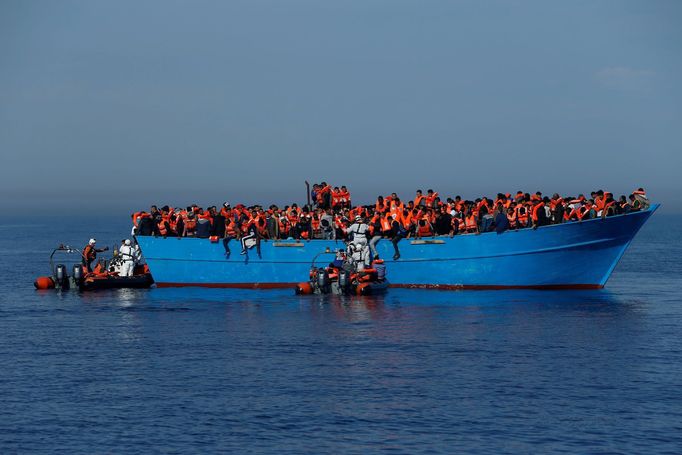 Humanitární pomocníci zachraňují uprchlíky z pašerácké lodě.