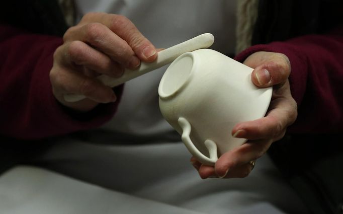 A worker uses a polishing stone to remove rough edges on a partially fired cup in the "biscuit room" at the Middleport pottery in Stoke-on-Trent, central England January 22, 2013. The pottery which dates back to 1888 and was rescued from closure in 2009, continues to use traditional methods to produce its range of ceramics and famous Burleigh Ware pottery. REUTERS/Phil Noble (BRITAIN - Tags: BUSINESS EMPLOYMENT SOCIETY) Published: Led. 22, 2013, 5:27 odp.