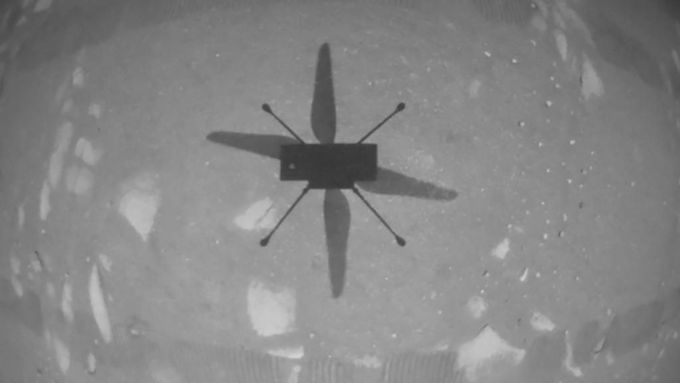 Na první fotografii z kamery na helikoptéře Ingenuity namířené směrem na zem je vidět stín vznášejícího se stroje.