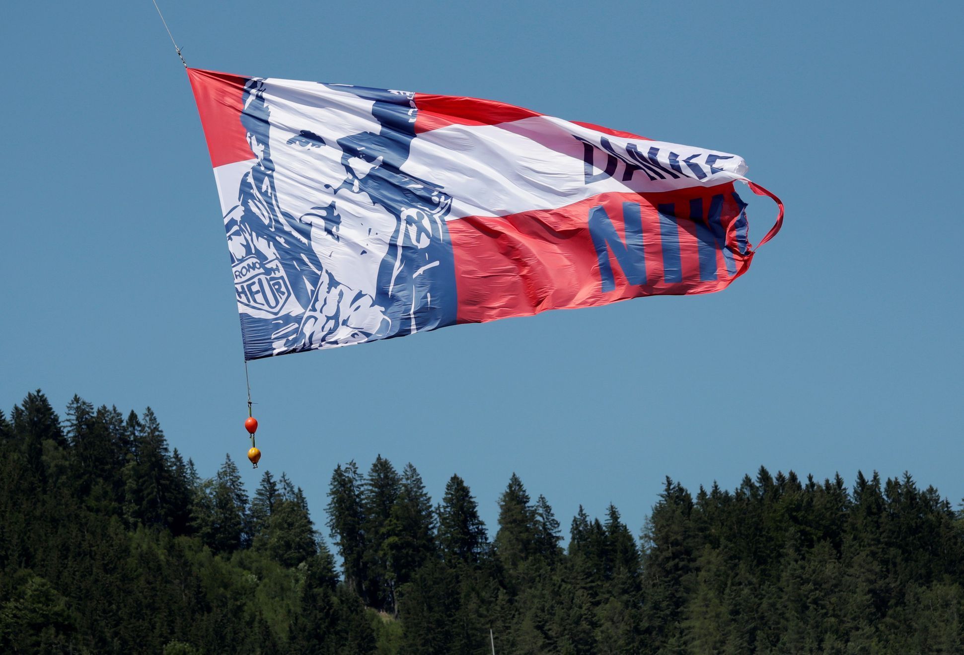 Vlajka s portrétem Nikiho Laudy nad Red Bull RIngem před startem VC Rakouska formule 1 2019
