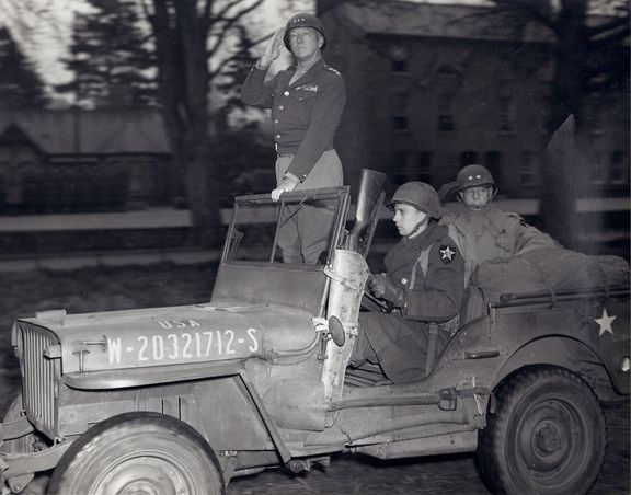 Generálové George S. Patton (stojící) a Walter Robertson při přehlídce v dubnu 1944.
