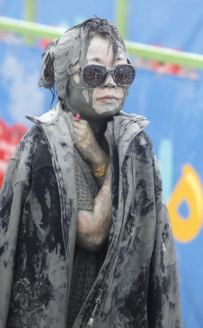 A woman wears a jacket to warm herself during the Boryeong Mud Festival at Daecheon beach in Boryeong, about 190 km (118 miles) southwest of Seoul, July 15, 2012. About 2 to 3 million domestic and international tourists visit the beach during the annual mud festival, according to the festival organisation. REUTERS/Lee Jae-Won (SOUTH KOREA - Tags: SOCIETY TRAVEL) Published: Čec. 15, 2012, 7:05 dop.