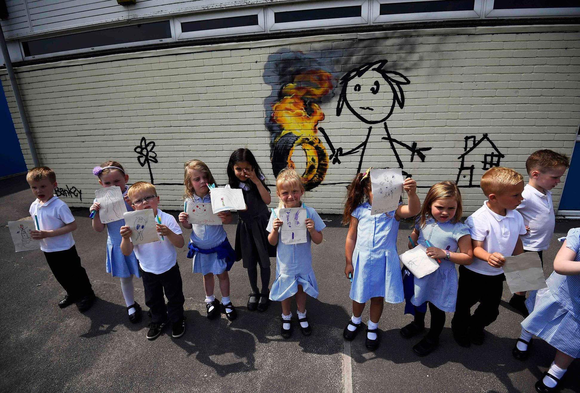 Reception class school children show off their drawings of a mural attributed to Banksy in Bristol