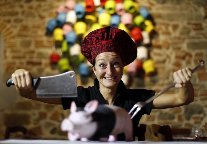 Italian chef Cristina Palanti poses with a meat cleaver and cooking fork hovering over a plastic pig figurine at the "L'e'Maiala" restaurant in Florence October 6, 2012. At walking distance from the tourist cafeterias around Palazzo Vecchio, Faggioli and her husband Frank are busy bartering wine and potatoes for a meal of Tuscan "pici" pasta with pork sauce. The neighbourly couple have recently launched a 40-seat restaurant in Florence that allows customers to exchange vegetables and used goods for a traditional Tuscan dinner, in a way to encourage people to dine out despite the recession. Picture taken October 6, 2012. To match story ITALY-BARTER/ REUTERS/Alessandro Bianchi (ITALY - Tags: SOCIETY BUSINESS FOOD) Published: Říj. 10, 2012, 9:11 dop.