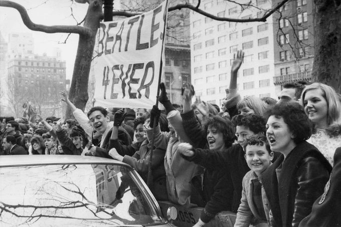 Křičící teenageři mávají transparentem "Beatles forever" na uvítanou britské kapele The Beatles z Liverpoolu před hotelem Plaza v New Yorku, USA, 7. únor 1964