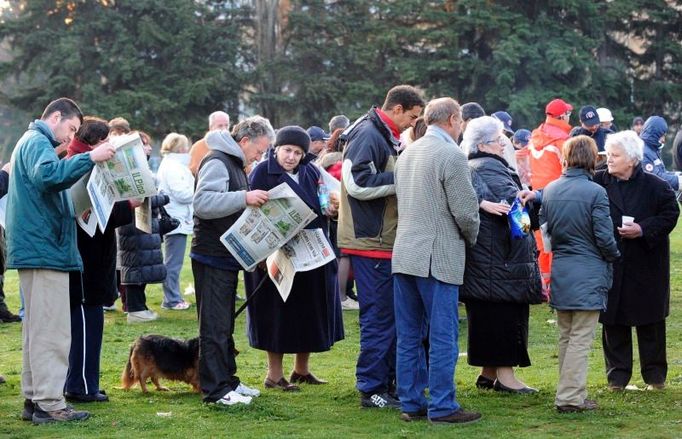 Fronta na horký čaj v táboře na stadionu v Aquile. Lidé si čtou čerstvé vydání novin a trpělivě čekají.