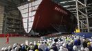 Workers watch as the forward section of the aircraft carrier HMS Queen Elizabeth is moved onto a barge at HM Naval Base in Portsmouth, southern England May 14, 2012. The hull will be transported by a sea going barge to Rosyth in Scotland where the ship will be assembled in dry dock. REUTERS/Luke MacGregor (BRITAIN - Tags: BUSINESS EMPLOYMENT MILITARY) Published: Kvě. 14, 2012, 2:20 odp.