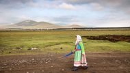 Tatjana Oslapova vyšňořená ve slavnostním kroji se vrací domů z nedělní ranní bohoslužby. Krajina kolem Gorelovky připomíná náhorní planiny v Tibetu.