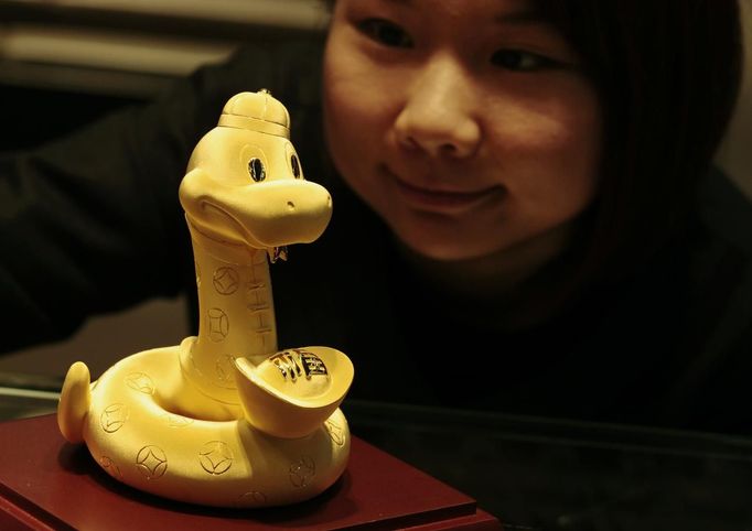 A staff member poses with a 24K gold sculpture in the shape of a snake carrying an ingot, designed for the year of the snake, at a jewellery store in Hong Kong January 29, 2013. The item weighs 5.219 Chinese taels (195 grams) and sells for HK$104,000 ($12,872). The Lunar New Year, also known as the Spring Festival, begins on February 10 and marks the start of the Year of the Snake, according to the Chinese zodiac. Picture taken January 29, 2013. REUTERS/Bobby Yip (CHINA - Tags: SOCIETY BUSINESS) Published: Úno. 8, 2013, 6:10 dop.