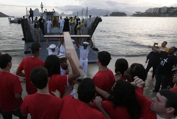 Catholics receive the World Youth Day cross from sailors of the Brazilian Navy during its arrival in Icarai beach in Niteroi near Rio de Janeiro May 19, 2013. Pope Francis will travel to Brazil on his first international trip as pontiff in July. The main purpose of the trip is for the pope to preside at the Catholic Church's World Day of Youth. The pope's participation in World Youth Day events starts on the evening of July 25 in Rio's famed Copacabana Beach area and culminates with a huge open-air Mass in the Guaratiba area of the city on July 28. REUTERS/Ricardo Moraes (BRAZIL - Tags: RELIGION SOCIETY) Published: Kvě. 19, 2013, 10:04 odp.