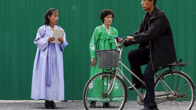 Cyklista a ženy v tradičních severokorejských krojích.