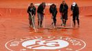 Workers sweep water off a tarp before a men's singles match between Martin Klizan of Slovakia and Kei Nishikori of Japan at the French Open tennis tournament at the Rolan