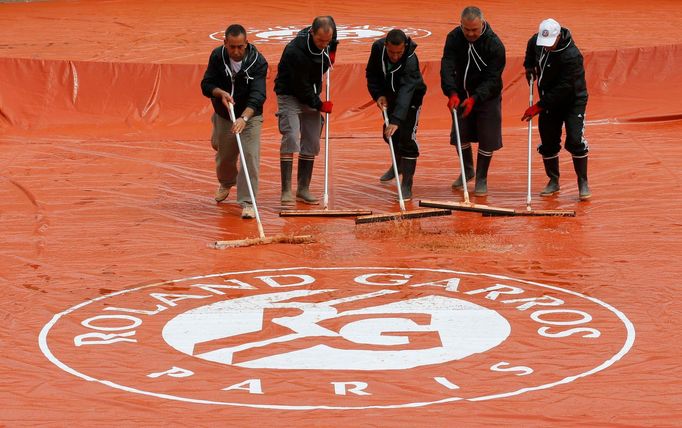 Workers sweep water off a tarp before a men's singles match between Martin Klizan of Slovakia and Kei Nishikori of Japan at the French Open tennis tournament at the Rolan