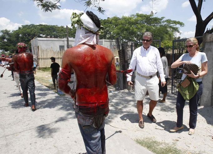 Tourists watch as penitents, bloodied after self-flagellation, walk during a Good Friday crucifixion re-enactment in San Pedro Cutud town, Pampanga province, north of Manila March 29, 2013. About two dozen Filipinos were nailed to crosses on Good Friday in an extreme display of devotion that the Catholic church looks down upon as a form of folk religion but appears powerless to stop. Holy Week is celebrated in many Christian traditions during the week before Easter. REUTERS/Romeo Ranoco (PHILIPPINES - Tags: RELIGION SOCIETY) Published: Bře. 29, 2013, 10:18 dop.