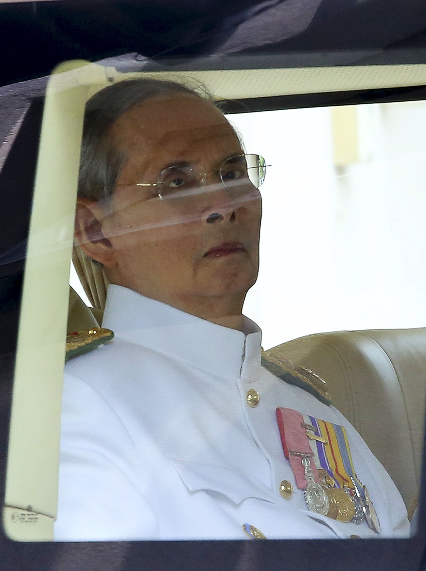 Thailand's King Bhumibol sits in a vehicle as he leaves Siriraj Hospital for the Grand Palace to join a ceremony marking coronation day in Bangkok
