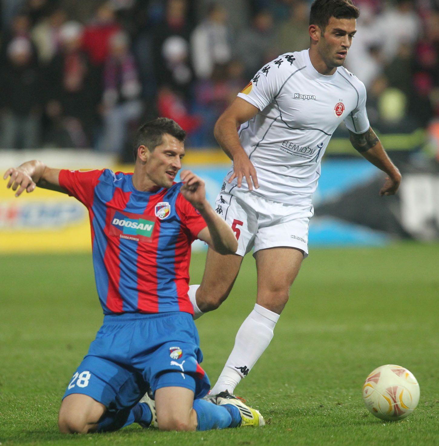 Fotbalista Plzně Marián Čišovský padá v souboji s Hananem Mamanem v utkání proti Hapoelu Tel Aviv během Evropské ligy 2012/13.