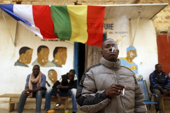 A Malian man smokes a cigarette in front of a shop with Malian and French flags hung outside in Timbuktu January 31, 2013. Mali's president offered Tuareg rebels talks on Thursday in a bid for national reconciliation after a French-led offensive drove their Islamist former allies into mountain hideaways. REUTERS/Benoit Tessier (MALI - Tags: POLITICS CIVIL UNREST CONFLICT TPX IMAGES OF THE DAY) Published: Led. 31, 2013, 7:04 odp.