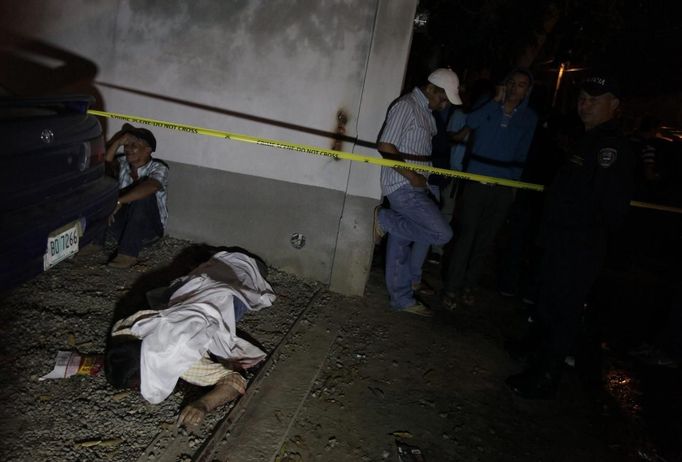 A man (L) mourns next to the body of a slain relative at a crime scene in the city of San Pedro Sula March 22, 2013. Unknown assailants killed three men and one woman on Friday at the crime scene in a working class neighbourhood, local media reported. San Pedro Sula has been labelled the most violent city on the planet, according to a U.N. Development Program report last week. Picture taken March 22, 2013. REUTERS/Jorge Cabrera (HONDURAS - Tags: CIVIL UNREST CRIME LAW) Published: Bře. 23, 2013, 9:02 odp.