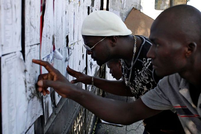 Seznamy voličů. Lidé v Port-au-Prince se hledají na listech před provizorní volební místností. Patří sem? Mají volit tady?