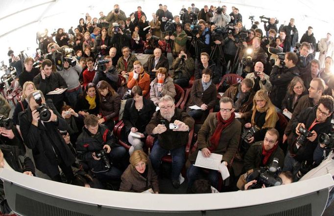 Novináři sledují proces na obrazovkách v mediálním stanu.