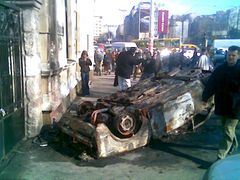 Převrácené ohořelé auto zůstalo po nočním řádění demonstrantů před vyrabovaným McDonaldem na Trgu Slavija v Bělehradě. (foto z mobilního telefonu)