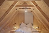 Ložnice pro hosty, která se nachází v druhé chatce se saunou, působí také velmi minimalisticky. Světlé dřevo doplňuje jen postel a noční stolky.
