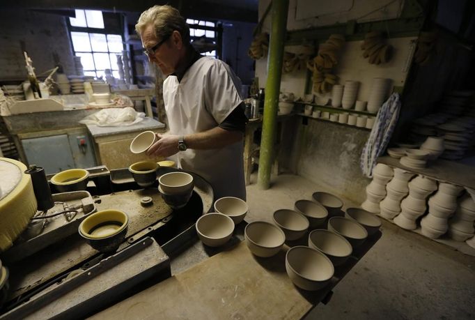 A worker removes bowls from a machine at the Middleport pottery in Stoke-on-Trent, central England January 22, 2013. The pottery which dates back to 1888 and was rescued from closure in 2009, continues to use traditional methods to produce its range of ceramics and famous Burleigh Ware pottery. REUTERS/Phil Noble (BRITAIN - Tags: BUSINESS EMPLOYMENT SOCIETY) Published: Led. 22, 2013, 5:39 odp.