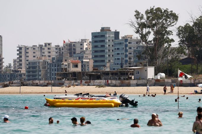 Lidé na pláži ve městě Famagusta, za nimi v dálce opuštěné paneláky ve Varoši.