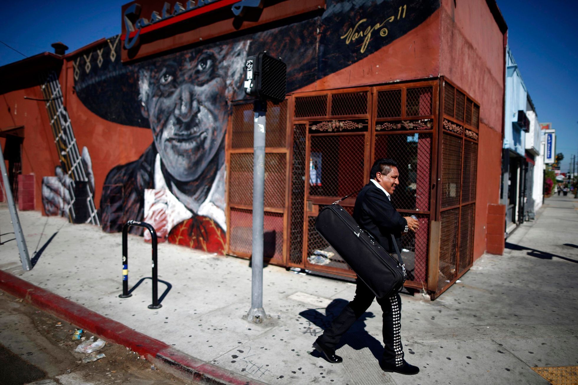 Mariachi musician walks past a mural in the Boyle Heights area of Los Angeles, home to many Mexican migrants, in California
