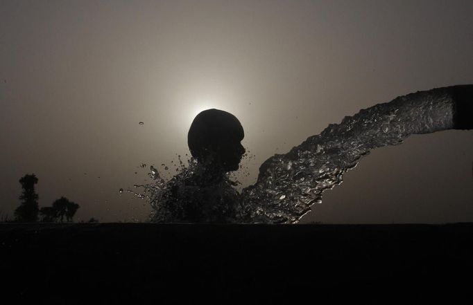 A boy is silhouetted against the setting sun as he cools himself off under a pipe during a hot day in Faisalabad on June 27, 2012. Temperatures reached 40 degrees Celcius (104 degrees Fahrenheit) in Faisalabad and the weather remained hot in some other parts of the country, the Pakistan Meteorological Department said on their website. REUTERS/Fayyaz Hussain (PAKISTAN - Tags: SOCIETY ENVIRONMENT) Published: Čer. 27, 2012, 3:55 odp.