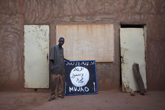 Hotel worker Abderrahmane Toure poses for a picture next to a sign for radical Islamist group Movement for Unity and Jihad in West Africa (MUJAO) in Douentza January 28, 2013. The sign reads, "There is no God but Allah and Mohammad is his prophet." REUTERS/Joe Penney (MALI - Tags: RELIGION CIVIL UNREST POLITICS CONFLICT) Published: Led. 28, 2013, 8:32 odp.