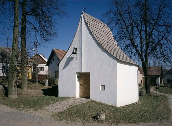 V Santiniho stopách Kaple Panny Marie Královny Jestřebí u Brtnice (okres Jihlava) Kuba & Pilař architekti, 1998  Nenápadná drobná kaplička si nečekaně vydobyla přízeň řady historiků architektury, kteří ji v různých anketách řadí na seznam top-ten staveb realizovaných v prvním desetiletí po sametové revoluci. Minimalistická vesnická stavba vzbudila zřejmě sympatie v protikladu k některým přezdobeným bankám a hotelům rané postmoderny devadesátých let. Jejími autory byli tehdy mladí brněnští architekti Ladislav Kuba a Jan Pilař, kteří vyhráli řadu prestižních architektonických soutěží (např. na knihovnu Filozofické fakulty Masarykovy Univerzity v Brně či na Západočeskou galerii v Plzni). Pro venkovskou kapli museli nejprve najít důstojné místo ve středu obce - v Jestřebí nikdy žádný svatostánek nestál, mše se sloužily pod širým nebem. Umístili ji na náves mezi dvě mohutné lípy, kde bývala stará hasičská zbrojnice. Stavbu provedli svépomocí místní občané.