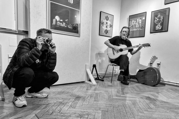 Fotograf Jiří Hanke hraje a zpívá na výstavě svých koláží. Muž s fotoaparátem je jeho syn Michael, také vynikající fotograf.
