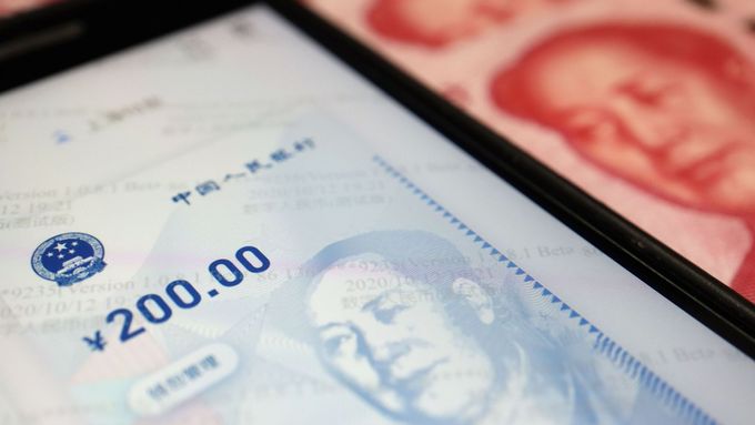 Snímek ukazuje čínskou aplikaci pro používání digitálního jüanu. V pozadí jsou vidět běžné papírové bankovky s oficiálním čínským platidlem.