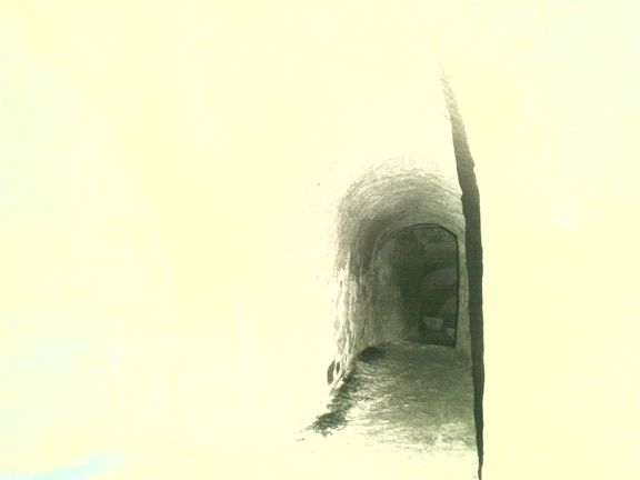 Upravený pohled do podzemní chodby, z šera vystupuje další klenutá komora a v ní snad cínová truhla.