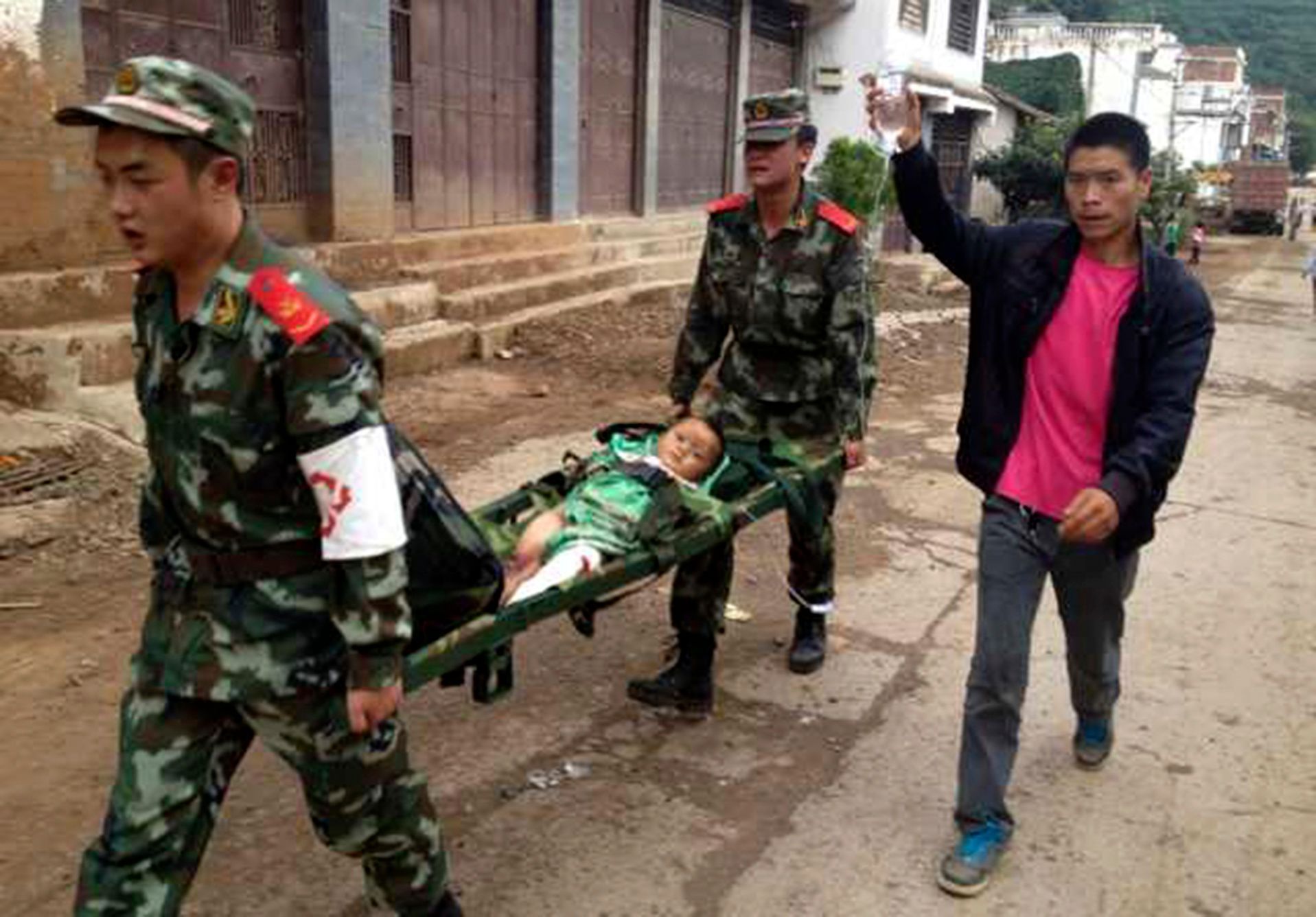 Policisté nesou zraněné dítě po zemětřesení v regionu Ludian