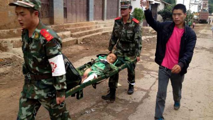 Policisté nesou zraněné dítě po zemětřesení v regionu Ludian.