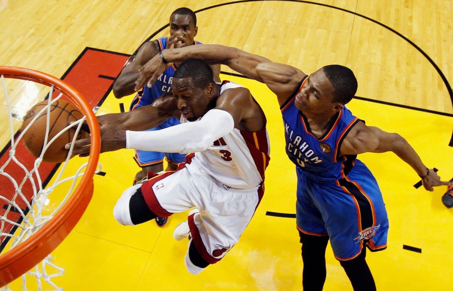 Basketbalista Dwayne Wade z Miami se snaží zavěsit přes bránící Russella Westbrooka (vpravo) a Kendricka Perkinse z Oklahomy ve finále play-off NBA 2012.
