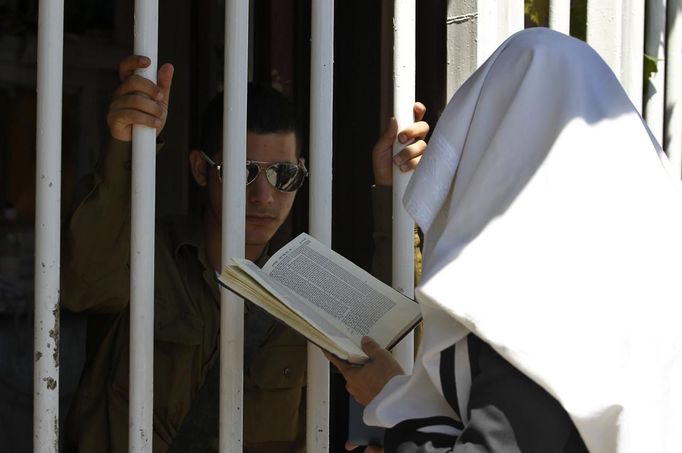 An ultra-Orthodox Jewish man covered by a prayer shawl (R) talks to a soldier at the entrance to a recruiting office in Jerusalem July 4, 2012. Prime Minister Benjamin Netanyahu's largest coalition partner issued a veiled threat on Wednesday to quit the government over a dispute about a bid to amend Israel's compulsory draft policy opposed by the powerful ultra-Orthodox community. REUTERS/Baz Ratner (JERUSALEM - Tags: POLITICS RELIGION) Published: Čec. 4, 2012, 2:46 odp.