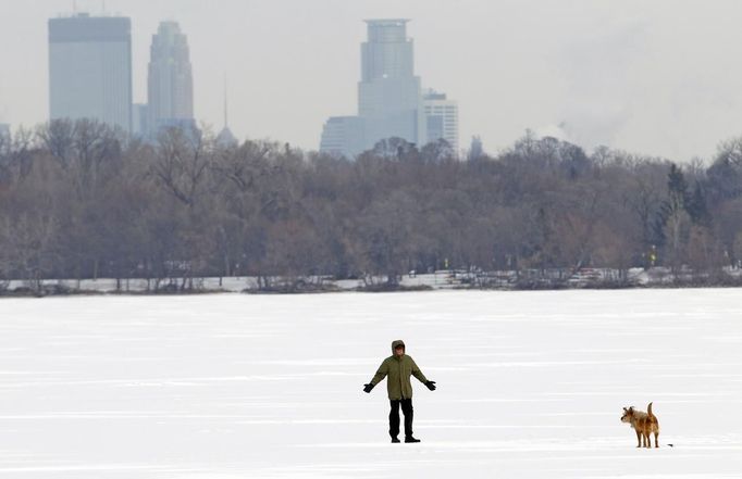 A man walks his dog across Lake Harriet near Minneapolis (background) January 23, 2013. The Upper Midwest remains locked in a deep freeze, with bitter sub-zero temperatures and wind chills stretching into a fourth day across several states due to waves of frigid Arctic air. REUTERS/Eric Miller (UNITED STATES - Tags: ENVIRONMENT) Published: Led. 23, 2013, 8:04 odp.