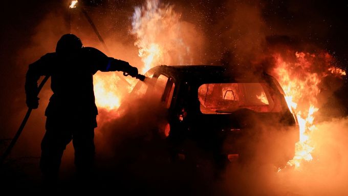 Francouzský hasič hasí hořící auto během pátého dne protestů po smrti sedmnáctiletého mladíka.
