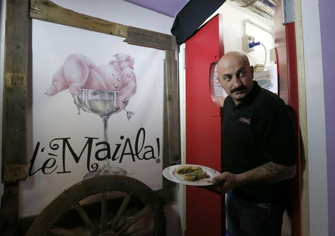 Francesco Francini, called Frank, husband of restaurant co-owner Donella Faggioli, carries a plate at the "L'e'Maiala" restaurant in Florence October 6, 2012. At walking distance from the tourist cafeterias around Palazzo Vecchio, Faggioli and her husband are busy bartering wine and potatoes for a meal of Tuscan "pici" pasta with pork sauce. The neighbourly couple have recently launched a 40-seat restaurant in Florence that allows customers to exchange vegetables and used goods for a traditional Tuscan dinner, in a way to encourage people to dine out despite the recession. Picture taken October 6, 2012. To match story ITALY-BARTER/ REUTERS/Alessandro Bianchi (SOCIETY BUSINESS FOOD) Published: Říj. 10, 2012, 9:41 dop.