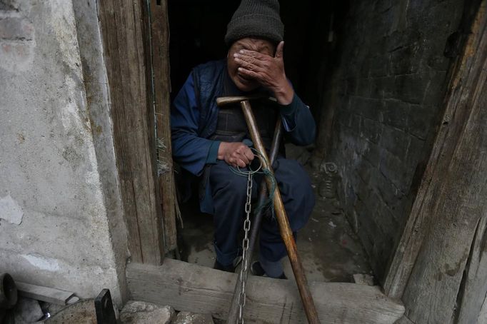 A boy's grandfather wipes away tears from his eyes as he holds onto the chain that is locked around the boy's ankle at their home in Zhejiang province