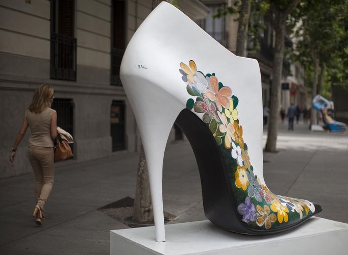 A woman in high heels passes a giant shoe figure which is part of an exhibition entitled Shoe Street Art in Madrid's high-end shopping district June 19, 2012. The street art exhibition is a homage to the entrepreneur spirit of Spanish shoe companies and part of a campaign for Spanish shoes. REUTERS/Paul Hanna (SPAIN - Tags: SOCIETY BUSINESS) Published: Čer. 19, 2012, 1:42 odp.