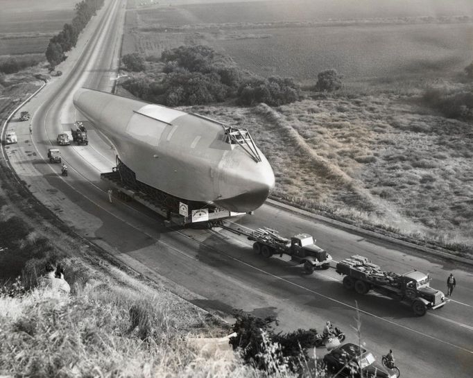 Trup letounu Hughes H-4 Hercules na transportním přívěsu, který je tažen po dálnici mezi hangáry továrny v Culver City a terminálem na Long Beach. Rok 1945