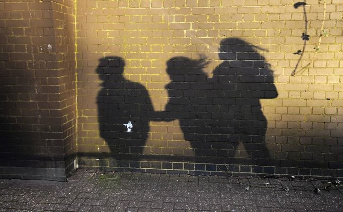 A shadow is cast on a wall of George Kapetanios, his wife and their daughter as they walk along a street in Potters Bar, on the outskirts of London