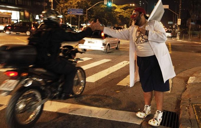 A member of the Traffic Psychologists greets a motorcyclist while performing in front of a traffic light in Sao Paulo July 23, 2012. Traffic Psychologists is a non-profit non-governmental organization which aims to humanize traffic and reduce the level of stress caused to drivers. Sao Paulo has more than 7 million vehicles, according to figures from the state transport authority Detran. Picture taken July 23, 2012. REUTERS/Nacho Doce (BRAZIL - Tags: TRANSPORT SOCIETY) Published: Čec. 24, 2012, 7:16 dop.